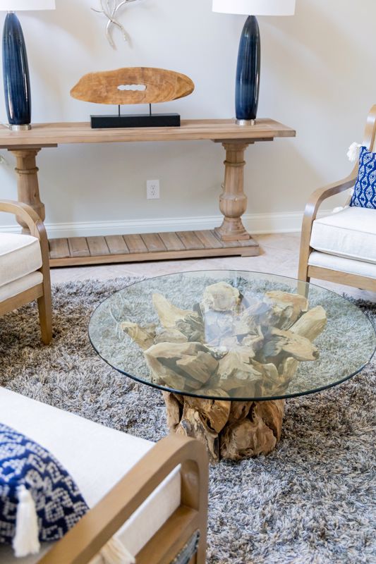 circular glass coffee table with natural wood base in front of side table with decorations