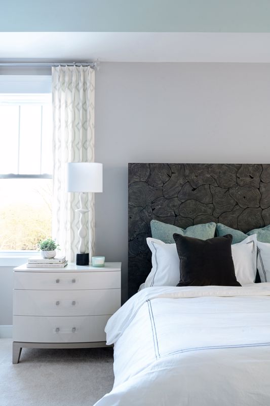 minimalist white bed and nightstand with dark gray headboard set against white wall and curtains