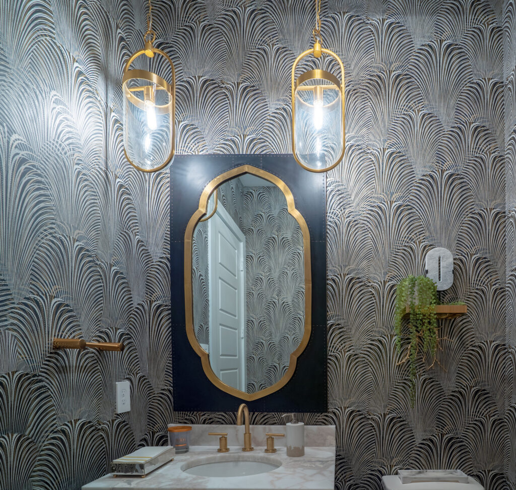 elegant bathroom vanity with gold trim mirror and lights set against intricate decorative floral pattern wallpaper