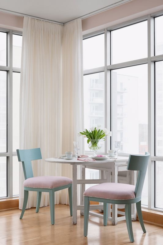 muted pastel colored chairs with white table set against tall windows and lace curtains window treatment