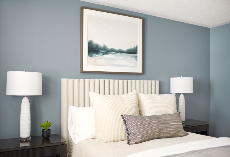 off-white linens and pillows with two white lamps set against gray-blue bedroom wall showcasing a cozy and cool summer interior design