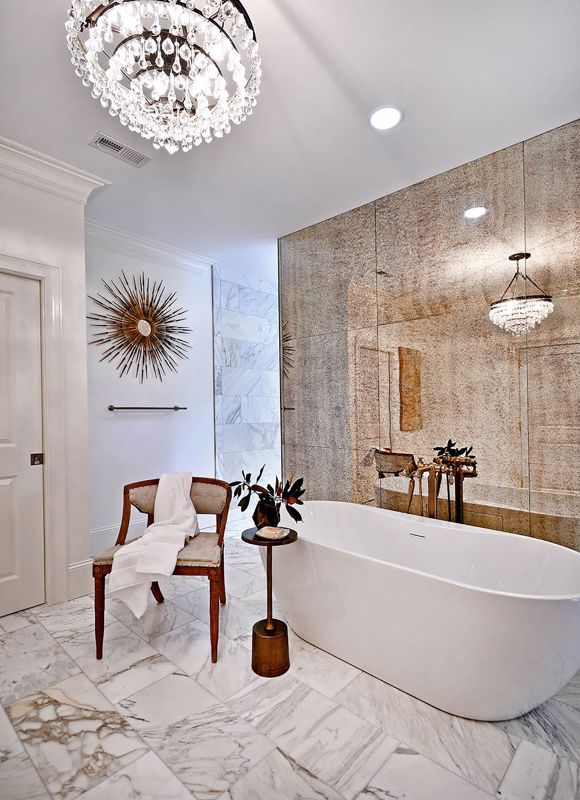 modern tub with vintage chair set on top of marble tile flooring with overhead chandelier showcasing a modern vintage bathroom in OH